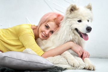 Charming pretty girl looking at camera and hugs her dog, young woman smiles widely and shows beautiful white teeth. A huge white dog looks into distance, his tongue, it hot from the arms of the owner.