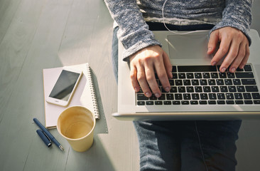 The young woman is sitting on the floor and working with laptop