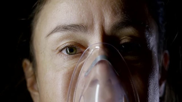 close up shot of the woman's face, who holds a tube from the inhaler near her mouth, steam comes through her