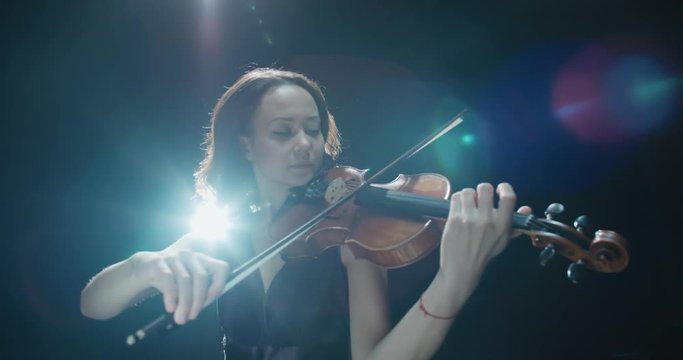 Violinist girl performing on stage, light, dark background