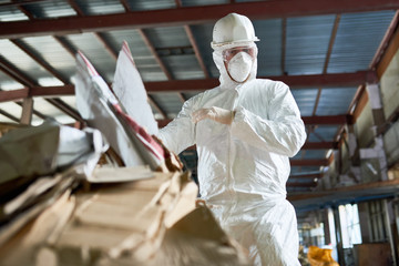 Low angle portrait of factory worker wearing biohazard suit sorting reusable cardboard on waste processing plant, copy space - obrazy, fototapety, plakaty