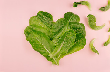Heart of fresh leaves greens salad on pink background. Cheerful modern spring food.