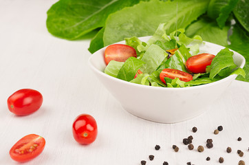 Healthy vegetarian spring salad -  fresh greens, tomatoes, pepper on white wood background, closeup, copy space.