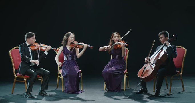 classical string quartet during the performance of the symphony, abstract black background in the studio