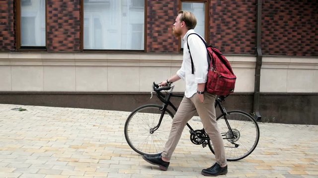 Slow motion footage of young hipster man walking with black vintage bicycle