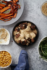Flatlay with traditional swedish beef meatballs with gravy served in one portion black cast iron pan, handle wrapped in blue towel, plates with sauce, baked carrots and chickpeas. Dinner concept.