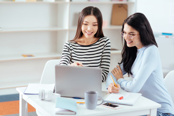 Productive work. Charming glad female colleagues  looking down while smiling and sitting on the chairs
