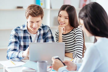 Together better. Joyful gay three students spending time together  while looking at the screens and sitting