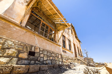Fototapeta premium Outside view of one of the abandoned houses in the ghost town of Kolmanskop near Lüderitz in Namibia, Africa. After the diamond rush ended, the houses are slowly getting swallowed by sand and dunes.