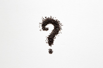 Question mark created from black, dried, loose tea with cup on the white table. Choice of the best...