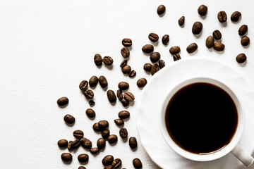 Cup of coffee with brown beans on the white table. Enjoying of coffee break at the work, at home, at visit with friends, family or alone everyday. Choice of the best sort and quality coffee.