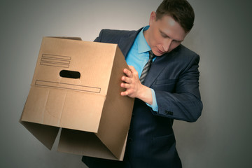 Businessman is holding a postage parcel in a cardboard box and shaking out of it something.