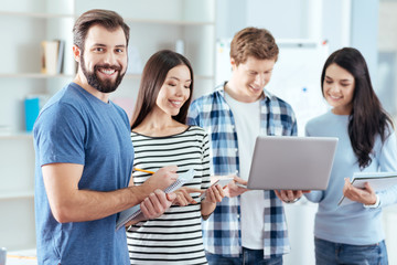  Common point. Satisfied good looking four colleagues sharing their opinions  while  man grinning and holding notebook