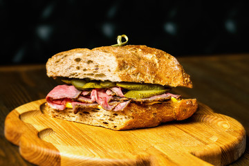 Closeup image of sandwich with meat and cucumbers at wooden board background.