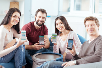 Modern opportunities. Young vigorous four friends posing on the light background  while demonstrating gadgets and  smiling to the camera