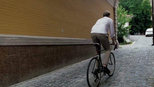 Slow motion steadicam video of young man riding vintage bicycle in passage way with paved road