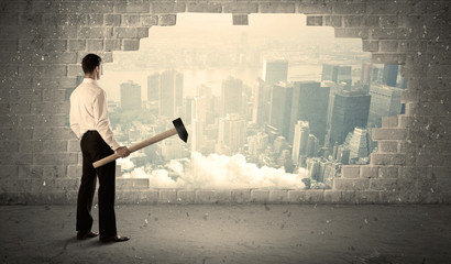 Business man hitting wall with hammer on city view