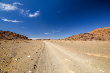 Beautiful wide angle view of a gravel road in the Namibian Desert and mountains in the background between Vioolsdrift and Aussenkehr near the South African border. Blue sky and beautiful clouds.