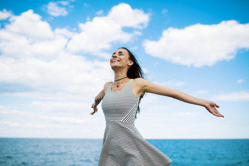 Fototapeta na wymiar I am free. Young attractive woman with long black hair rejoices in the wind and smiles. Wonderful sky