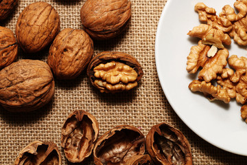 Walnuts, peel and white plate on the background of sacking.