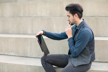 Young creative man sitting on the stairs with a modern tablet with a stylus pen in his hand