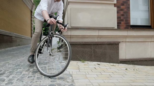 Slow motion video of stylish hipster man riding vintage bicycle out of narrow passageway on old street