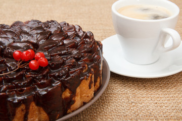 Chocolate cake decorated with bunch of viburnum and cup of coffee beside it