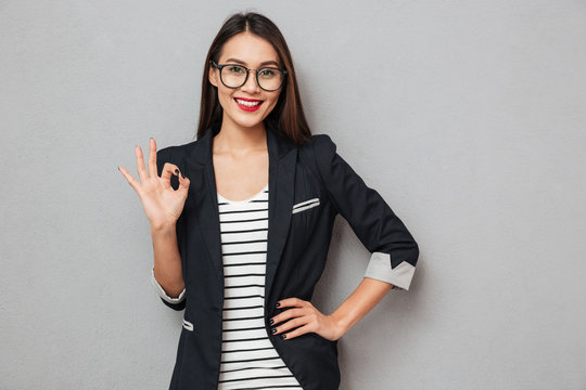 Smiling asian business woman in eyeglasses with arm on hip
