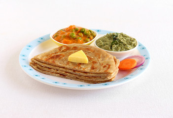 Kerala paratha, a type of Indian bread, sliced and stacked, with butter topping and carrot and onion salad, and bowls of peas and carrot curry and pudina chutney as side dishes.
