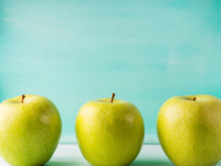 Three Green apples on turquoise background. Healthy food three pillars concept.