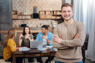 Handsome. Smart reliable worker standing with his arms crossed and smiling cheerfully while his...