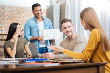 Interesting project. Cheerful smiling emotional student feeling excited while standing in front of his cheerful friends and waiting for them to discuss his interesting creative project