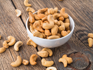 Cashew nuts in  white cup on brown wooden background, side view.