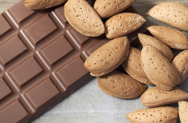Close up of a bunch of raw almonds in their shells on a bar of milk chocolate on wooden background