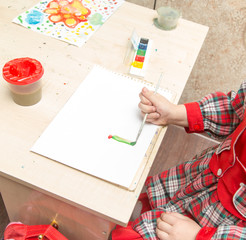 A girl draws a drawing with paints on a sheet