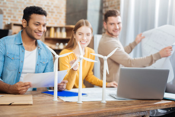 Tiny windmills. Cheerful young qualified engineers sitting at the table and looking at the tiny models of windmill turbines