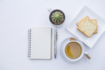 Blank notebook with hot tea and biscuit on white table background, tea break time