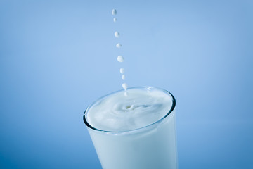 Milk glass with falling drops on blue background