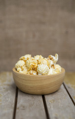 Fresh popcorn in wooden bowl on wooden table over blurred hessian texture background, snack time
