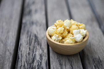 Salted popcorn in round wooden bowl on wooden table, snack for movie 