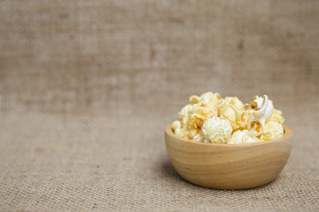 Salted popcorn in wooden bowl over blurred hessian texture background, movie snack