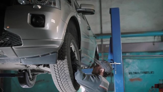 The vehicle repair technician wields the previously discarded wheel on the car, he checked the vehicle's mechanisms for determining the breakdown