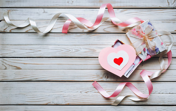A gift for Valentine's Day. Gift box with ribbons and hearts on a wooden background. Festive decor. Copy space.
