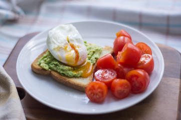 Perfect poached egg with avocado toast and fresh tomatoes on a white plate on a dish cloth