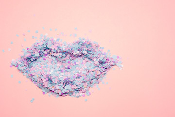 Lips shape made of blue, violet, pink confetti on pale pink textured paper background with space for text and design. Pop art style. 