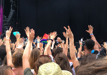 Audience with hands raised at a music festival, empty stage with copy space in the background