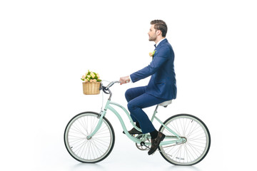 Obraz premium side view of groom in suit riding retro bicycle isolated on white
