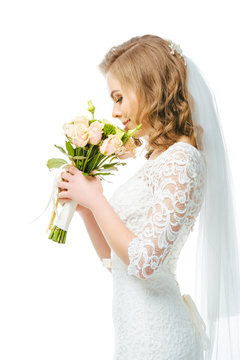 side view of attractive bride in wedding dress and veil with bouquet of flowers isolated on white