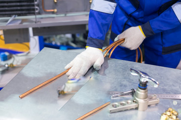 manufacturing, technology, factory concept. there is man who dressed in special blue uniform and gloves for protecting when he is working with welding, he is holding hank of copper thin tube