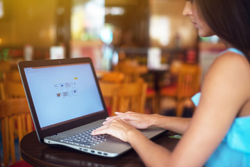 Side view of thin young brunette woman surfing the web on portable computer in empty restaurant.